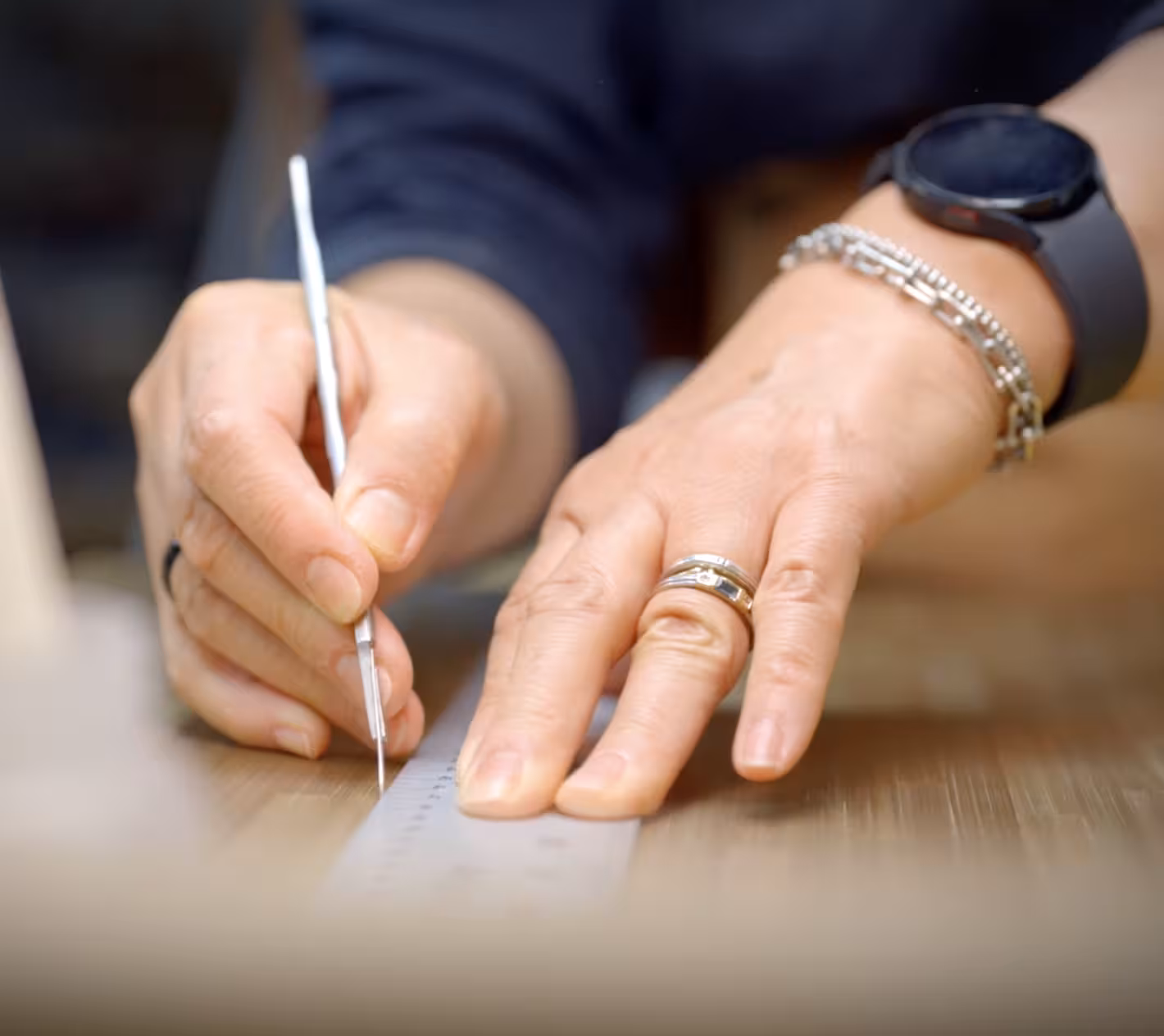 Close-up of a person marking measurements on a piece of wood with a pencil and ruler while wearing a watch and bracelets.