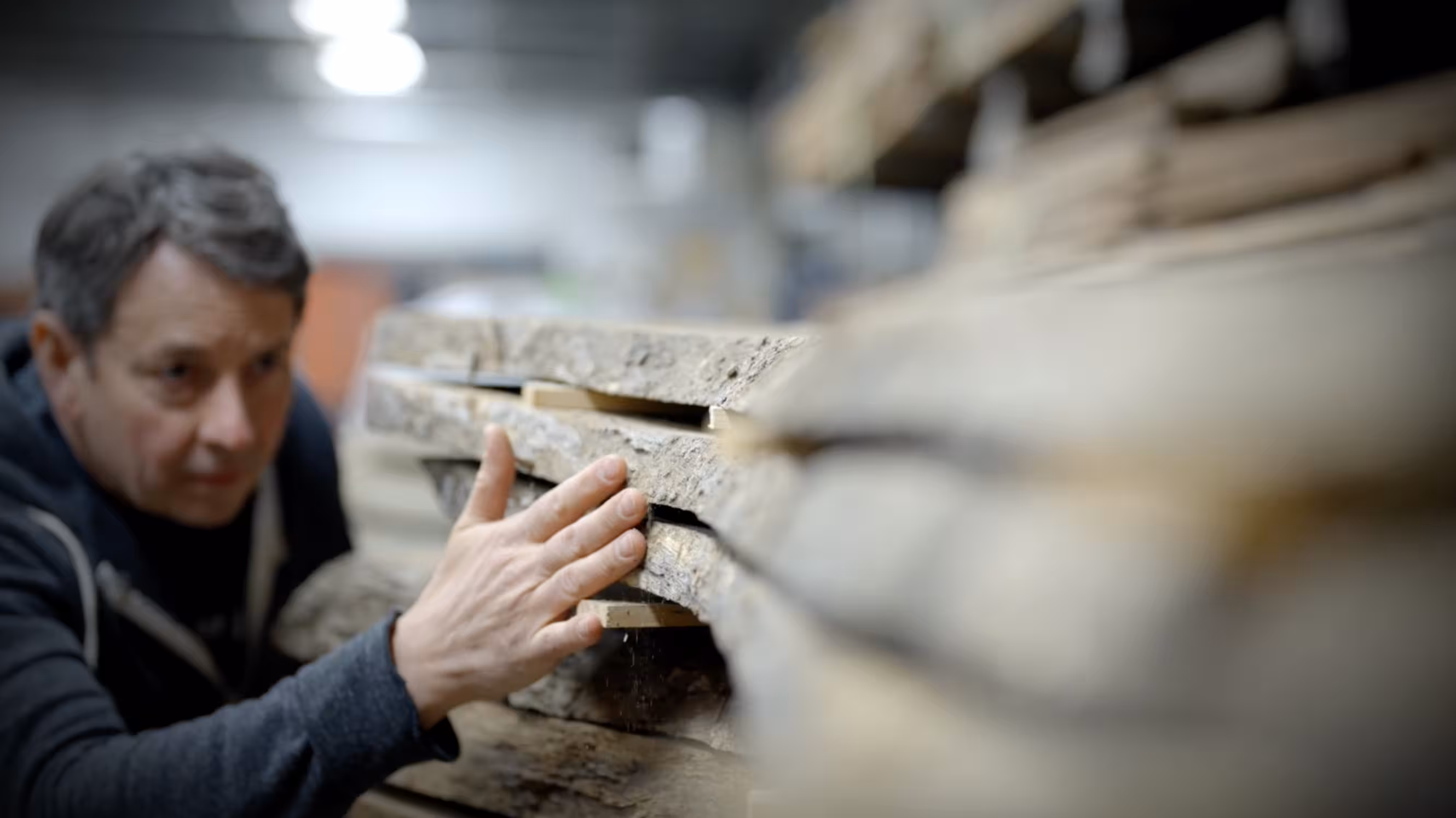 Man closely inspecting stacked wooden boards in a workshop environment.