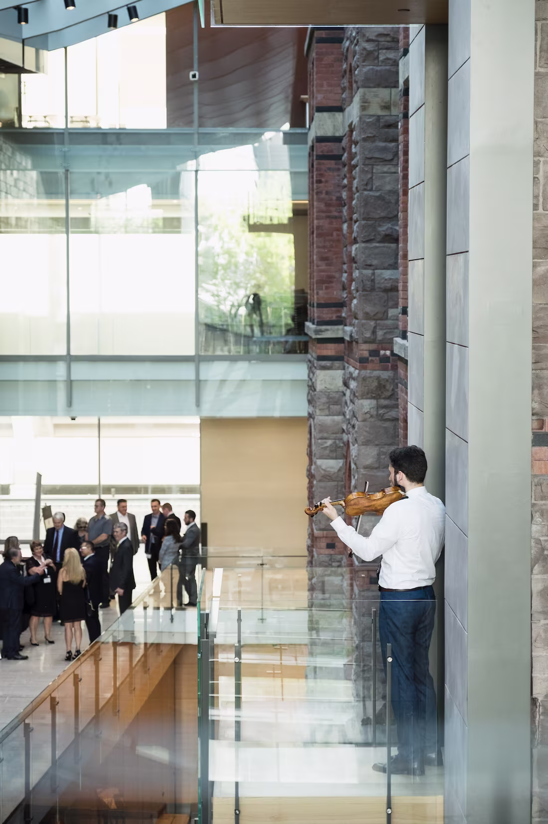 Violinist performing in a spacious indoor venue while guests gather and converse in the background.