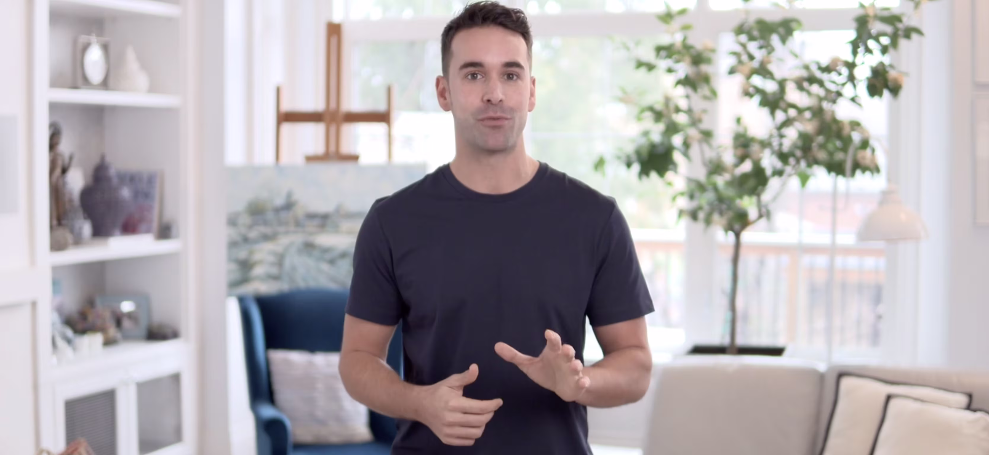 Man speaking directly to the camera in a bright living room setting, demonstrating or explaining a medical procedure.